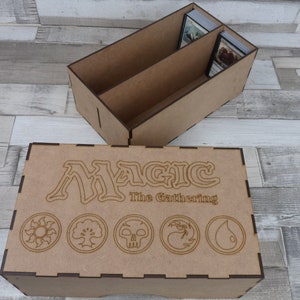May include: A wooden box with a Magic: The Gathering logo and five symbols on the lid. The box has two compartments inside for storing cards.