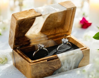 Op de afbeelding: Een houten ringendoos met een witte inlay en twee zilveren ringen met diamanten. De doos is open en de ringen liggen erin.