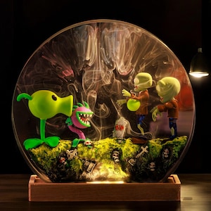 May include: A clear glass dome with a green, purple, and brown plant and three green zombie figurines inside. The dome is lit from the bottom, creating a glowing effect.