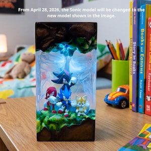 May include: A rectangular light-up display featuring Sonic the Hedgehog characters. The display includes Sonic, Tails, Knuckles, and Shadow figures. The text on the display reads, "From April 28, 2026, the Sonic model will be changed to the new model shown in the image."