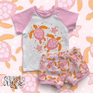 May include: A pink and white two-piece outfit for a child featuring a short-sleeved t-shirt with a graphic of two orange and pink sea turtles and a pair of pink and white shorts with a repeating pattern of orange and pink sea turtles.