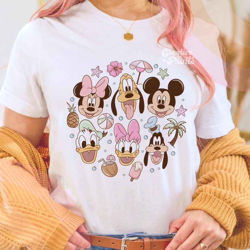 May include: White t-shirt with a colorful graphic print of Mickey Mouse, Minnie Mouse, Donald Duck, Daisy Duck, and Goofy. The characters are surrounded by summer-themed elements like palm trees, pineapples, and beach balls.