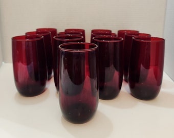 May include: A set of 12 deep red glass tumblers. The glasses are clear and have a slight lip around the rim.