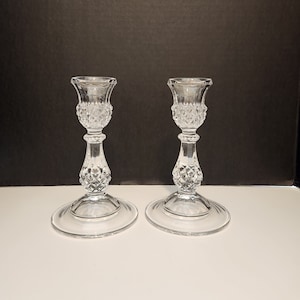 Peut inclure: Deux bougeoirs en verre transparent avec un motif en diamant. Les bougeoirs ont une base large et une tige haute et fine.
