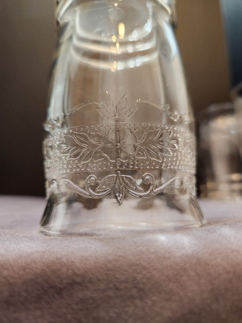 Puede incluir: Un tarro de vidrio transparente con un intrincado dise&ntilde;o floral grabado en el vidrio. El dise&ntilde;o presenta una flor central con hojas y un borde decorativo.