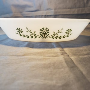 May include: White oval baking dish with a green floral design. The design features three stylized flowers with leaves and stems.