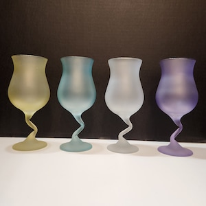 May include: Four frosted glass goblets in shades of yellow, blue, gray, and purple. Each goblet has a unique, twisted stem and a wide, rounded bowl. The glasses are arranged in a row against a black background.