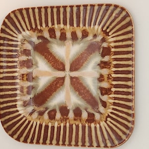 May include: A square ceramic dish with a brown and white geometric pattern. The dish has a raised rim with a striped design.