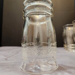 Puede incluir: Un vaso de beber de vidrio transparente con un patr&oacute;n floral decorativo alrededor del medio. El vaso tiene una base ancha y una parte superior ligeramente acampanada.