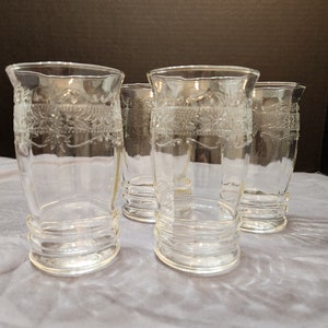 Puede incluir: Cuatro vasos de vidrio transparente con un dise&ntilde;o grabado decorativo. Los vasos tienen un fondo redondeado y una parte superior acampanada.