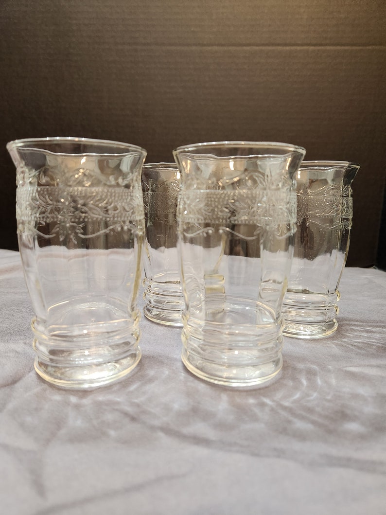Puede incluir: Cuatro vasos de vidrio transparente con un dise&ntilde;o grabado decorativo. Los vasos tienen un fondo redondeado y una parte superior acampanada.