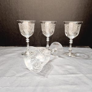 May include: Set of four clear glass stemmed wine glasses with an etched design. The glasses are arranged on a white tablecloth.