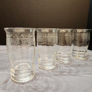 Puede incluir: Cuatro vasos de beber de vidrio transparente con un dise&ntilde;o grabado decorativo alrededor del borde superior.