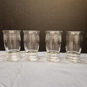Puede incluir: Juego de cuatro vasos de beber de vidrio transparente con un dise&ntilde;o grabado decorativo. Los vasos tienen una base redondeada y una parte superior cil&iacute;ndrica recta.