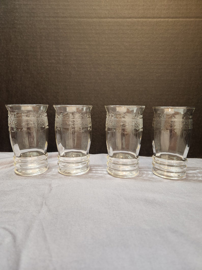Puede incluir: Juego de cuatro vasos de beber de vidrio transparente con un dise&ntilde;o grabado decorativo. Los vasos tienen una base redondeada y una parte superior cil&iacute;ndrica recta.