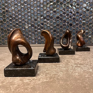 May include: Four abstract bronze sculptures on black bases. Each sculpture is a unique, organic shape with a smooth, polished finish.