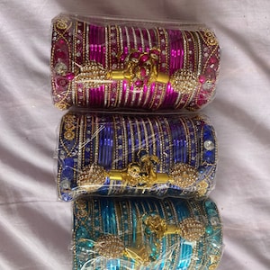 May include: Three sets of colorful bangles with gold accents and decorative embellishments. The bangles are packaged in clear plastic.