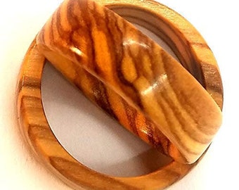 May include: Two interlocking olive wood rings, one with a wider band and a more intricate grain pattern. The rings are a natural light brown color with darker brown streaks.