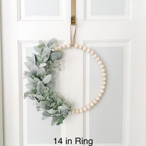 May include: A 14 inch wooden bead wreath with a green and white eucalyptus garland. The wreath is hanging on a white door.