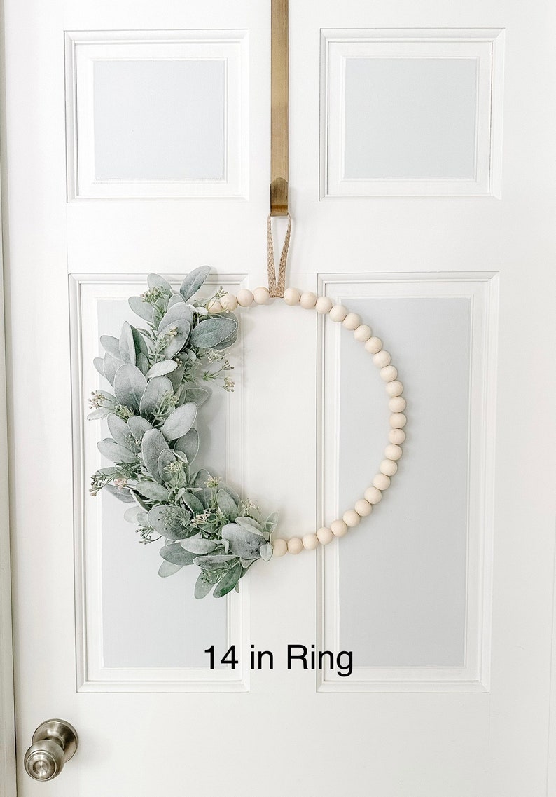 May include: A 14 inch wooden bead wreath with a green and white eucalyptus garland. The wreath is hanging on a white door.