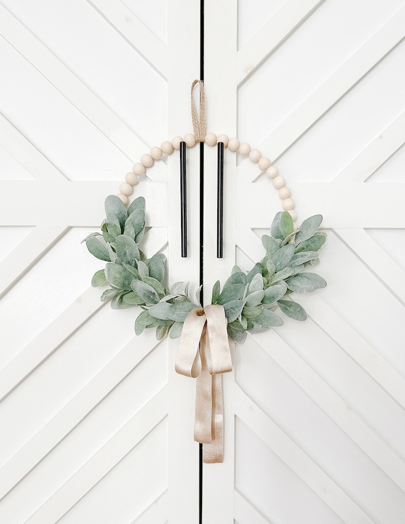May include: A wooden bead wreath with a green leafy garland and a gold ribbon hanging on a white door with a geometric pattern.