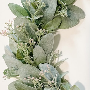 May include: A green and white eucalyptus garland with small pink flowers. The garland is made of artificial greenery and is perfect for adding a touch of nature to your home decor.