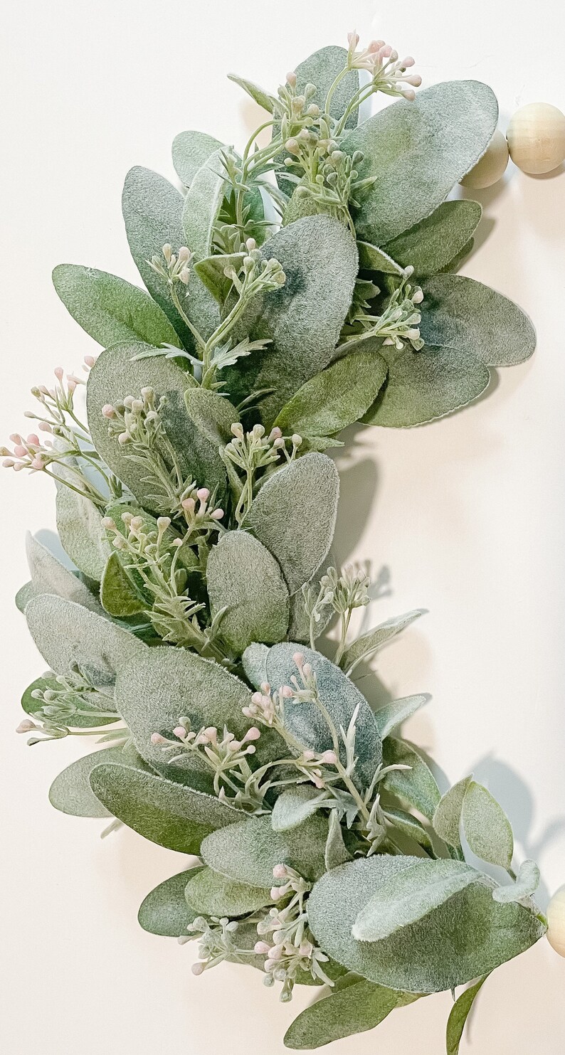 May include: A green and white eucalyptus garland with small pink flowers. The garland is made of artificial greenery and is perfect for adding a touch of nature to your home decor.