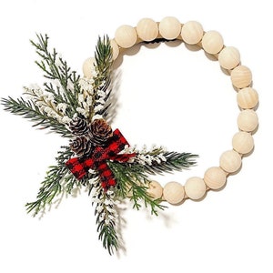 Puede incluir: Una corona circular de cuentas de madera, adornada con elementos festivos. Incluye ramas de pino verdes, acentos florales blancos y pi&ntilde;as marrones. Un lazo escoc&eacute;s rojo y negro proporciona contraste. Ideal para la decoraci&oacute;n de temporada.