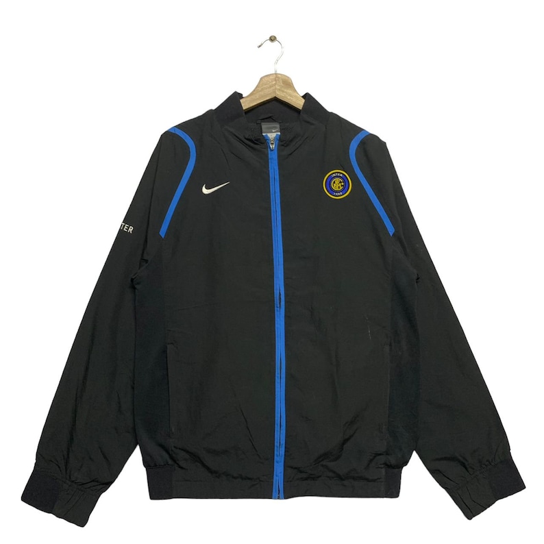 May include: Black zippered jacket with a blue zipper and trim. The jacket has a Nike swoosh logo on the left chest and a blue and gold Inter Milan logo on the right chest.
