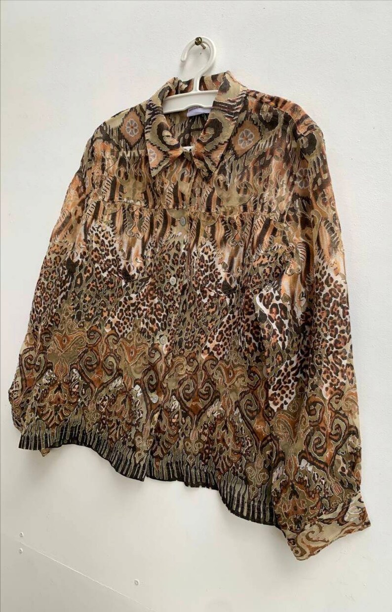 May include: A brown and beige patterned sheer button-up shirt with a collared neckline. The shirt has a long sleeve and a relaxed fit.
