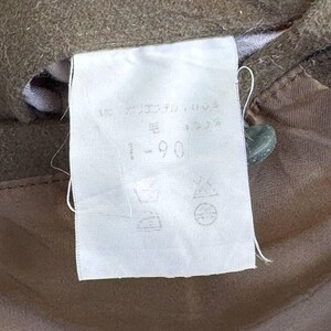 May include: A white fabric tag with black text that reads "90 - 毛", "15", and "35". The tag also has symbols for washing instructions. The tag is attached to a brown fabric.