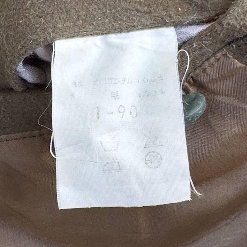 May include: A white fabric tag with black text that reads "90 - 毛", "15", and "35". The tag also has symbols for washing instructions. The tag is attached to a brown fabric.