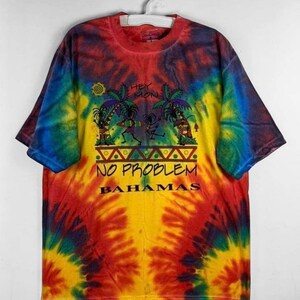 以下が含まれることがあります： カラフルなデザインのタイダイTシャツ。ヤシの木、棒人間、そして「Hey Mon No Problem Bahamas」というテキストが描かれています。