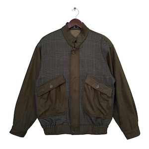 May include: A brown and green plaid bomber jacket with two large pockets on the front. The jacket has a zipper closure and a ribbed waistband.