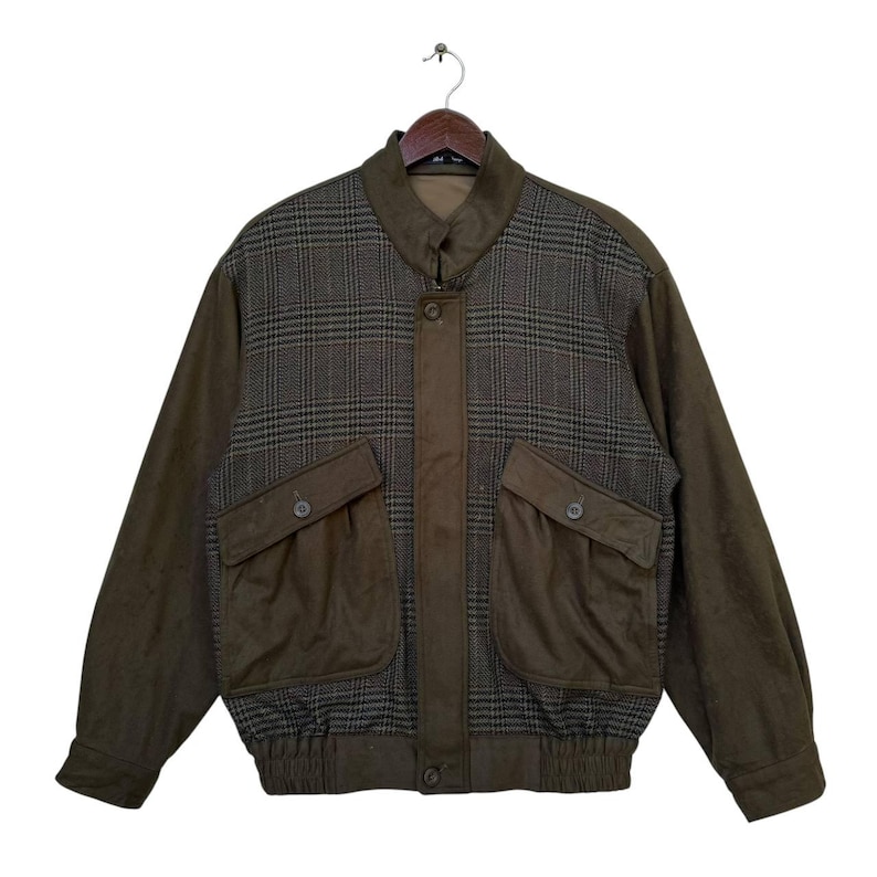 May include: A brown and green plaid bomber jacket with two large pockets on the front. The jacket has a zipper closure and a ribbed waistband.