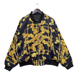 May include: A black bomber jacket with a gold chain and coin print. The jacket has a zipper closure and ribbed cuffs and waistband.