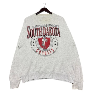 May include: A grey sweatshirt with a red and white graphic of the University of South Dakota Coyotes logo featuring a cartoon coyote. The logo includes the text "University of South Dakota Coyotes".