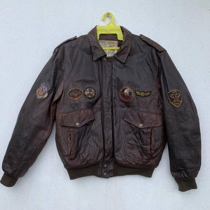 May include: A brown leather bomber jacket with multiple patches, including a US Air Force patch, a 357th Fighter Squadron patch, and a 1st Fighter Group patch.