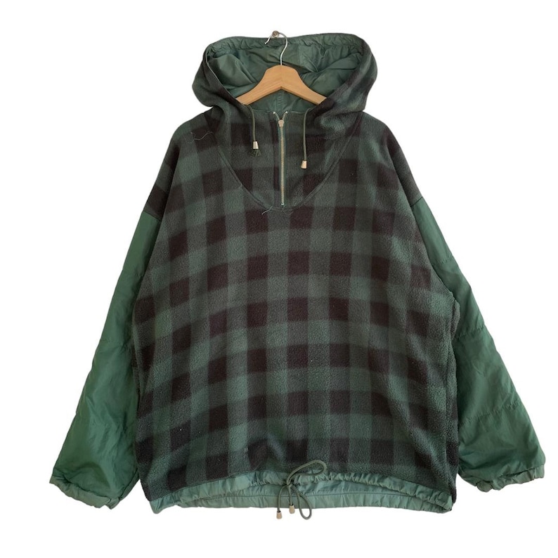 May include: A green and black plaid fleece pullover with a half-zip closure and a drawstring at the bottom. The sleeves are a solid green color.