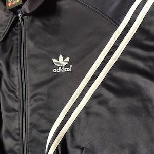 May include: A black satin jacket with white stripes and the Adidas logo on the front.
