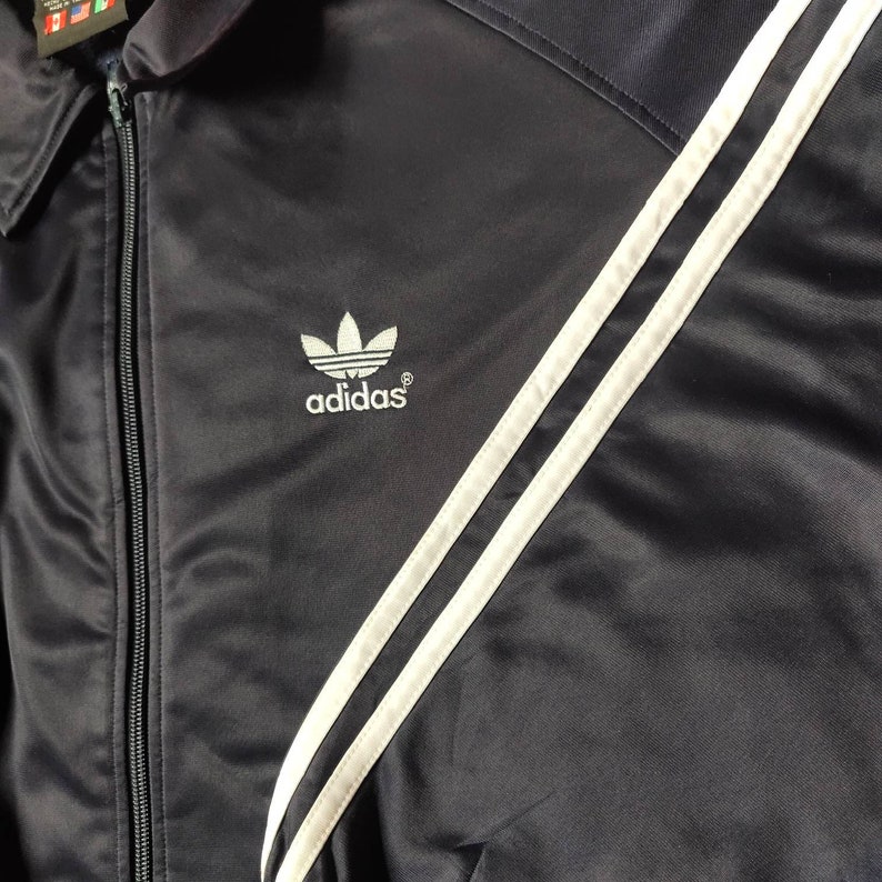 May include: A black satin jacket with white stripes and the Adidas logo on the front.