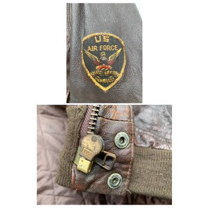 May include: Close-up of a brown leather jacket with a zipper and a US Air Force patch. The patch is embroidered with a winged eagle and the words "US Air Force".