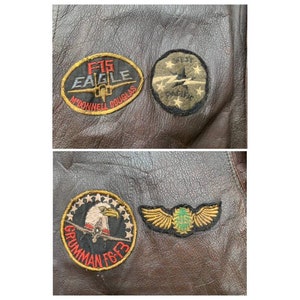 May include: A brown leather jacket with four embroidered patches. The patches are for the F-15 Eagle, McDonnell Douglas, 1st Fighter Squadron, and the US Air Force.