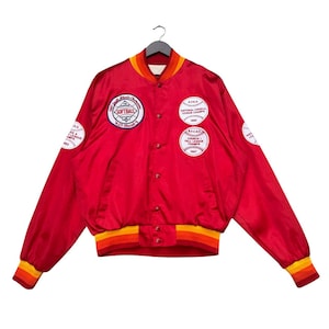 Pode incluir: Casaco de beisebol de cetim vermelho com patches bordados. Os patches apresentam as palavras "Softball", "National Church League Champs" e "Church I Fall League Champs".