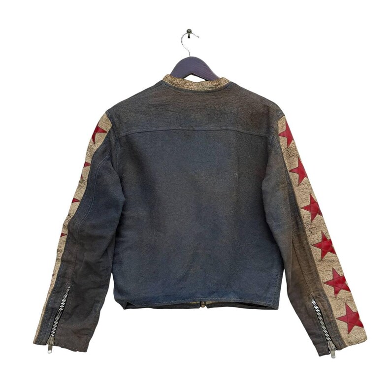 Op de afbeelding: Een donkerblauw denim jack met rode en bruine sterren op de mouwen. Het jack heeft een ritssluiting en een opstaande kraag.