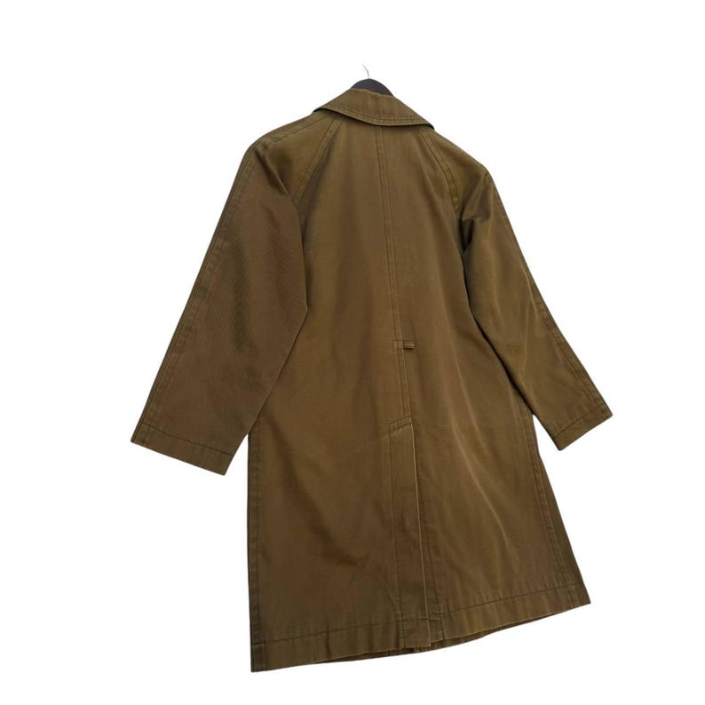 May include: An olive-green coat hangs from a black hanger. The coat has a classic collar, long sleeves, and a button closure. The back view of the coat is visible, showcasing its simple, tailored design. This outerwear piece is suitable for various occasions. The coat is a shade of green.