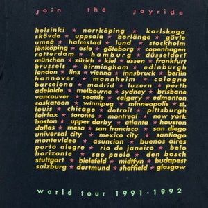 May include: Black t-shirt with white text listing cities around the world. The text reads "Join the Joyride World Tour 1991-1992".