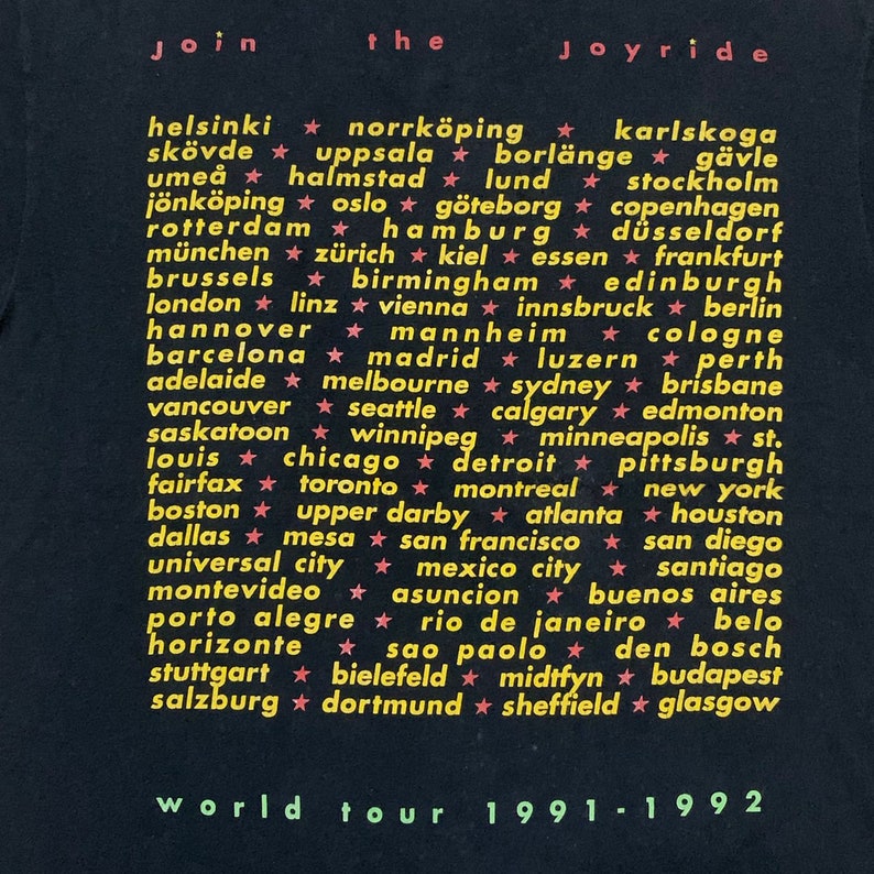 May include: Black t-shirt with white text listing cities around the world. The text reads "Join the Joyride World Tour 1991-1992".