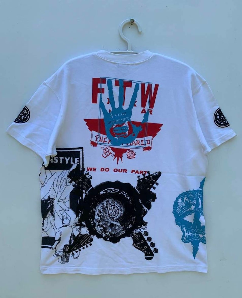 May include: White t-shirt with a graphic print of a hand with the text "FTW" and "4 year anniversary" in red and blue. The shirt also features a graphic print of a skull, guitars, and the text "We do our part".