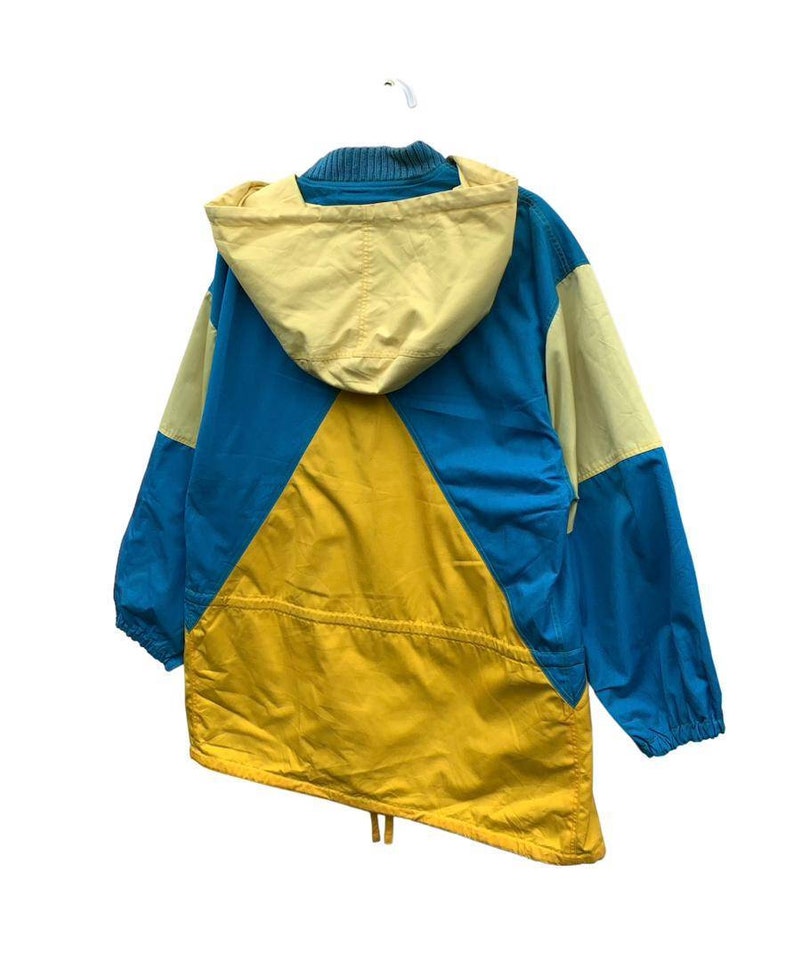 May include: A blue, yellow, and cream colored hooded jacket with a drawstring at the bottom.